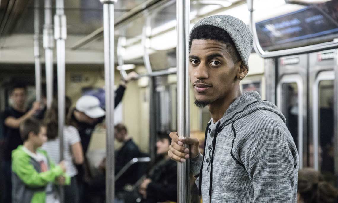 Man standing on public transportation holding safety pole with other passengers in the background
